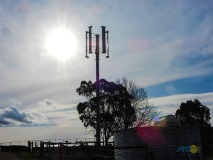 Vertical Axis Wind Turbine - VAWT silhouette at dusk, shows position above surrounding tree line.